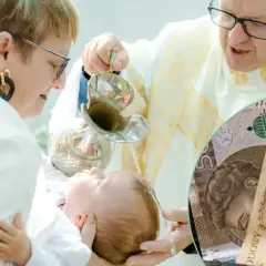 Chrzest dziecka, ksiądz polewa głowę wodą, a obok polskie banknoty. Ile pieniędzy na chrzest od dziadków?