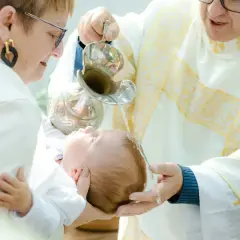 Chrzest dziecka. Kapłan polewa główkę niemowlęcia wodą święconą. Warto wiedzieć, ile kosztuje chrzest, by odpowiednio się przygotować.