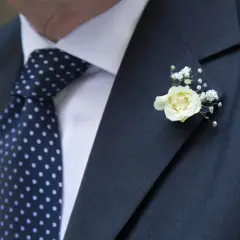 Elegancki garnitur z granatowym krawatem w kropki i delikatnym, białym kwiat w butonierce.