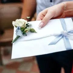 Biała koperta z błękitną wstążką i butonierką. Zastanawiasz się, ile chrzestny daje na wesele?