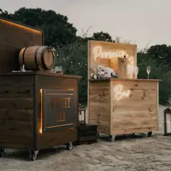Drewniane, mobilne bary na wesele: jeden z beczką whisky, drugi z napisem "Prosecco Bar". Idealne na letnie przyjęcie.