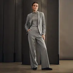 Elegancka kobieta w szarym garniturze, idealnym na wesele w spodniach. Stylowa i pewna siebie.
