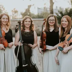 Uśmiechnięty kwartet smyczkowy pozuje z instrumentami na tle parku.