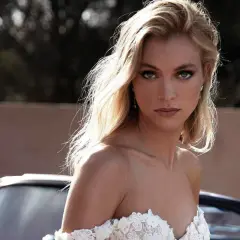 Olśniewająca panna młoda w sukni z koronki, z perfekcyjnym makijażem ślubnym glamour, pozuje przy stylowym samochodzie.
