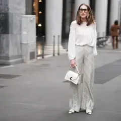 Elegancka kobieta w białej bluzce i srebrnych spodniach. Czy na komunie można ubrać się na biało? Ta stylizacja pokazuje, że tak, jeśli jest gustowna.