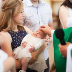 Chrzest dziecka, młoda kobieta trzyma niemowlę, a ksiądz namaszcza je. Czy rodzeństwo może być chrzestnymi?