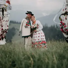Para młoda w strojach góralskich z kapelą w tle, na tle górskiego krajobrazu.