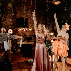 Radosny tłum świętuje oczepiny. Kobiety w pięknych sukniach unoszą ręce, a neonowy napis "Let's Dance!" zachęca do zabawy.
