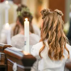 Chrzestny na komunii wspiera dziecko, trzymając zapaloną świecę.