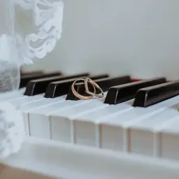 Dwa obrączki na klawiszach pianina, obok białej koronki.