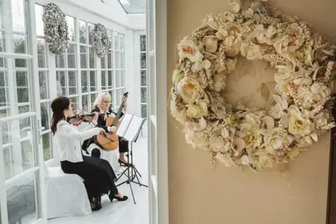 Dwie artystki grają na skrzypcach i gitarze, tworząc oprawę muzyczną ślubu. Cena takiej usługi zależy od wielu czynników.