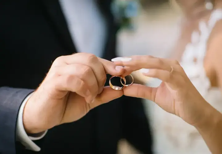 Dłonie pary trzymają obrączki, symbolizujące miłość i wierność. Na której ręce nosi się obrączkę? Tradycyjnie na serdecznym palcu lewej dłoni.