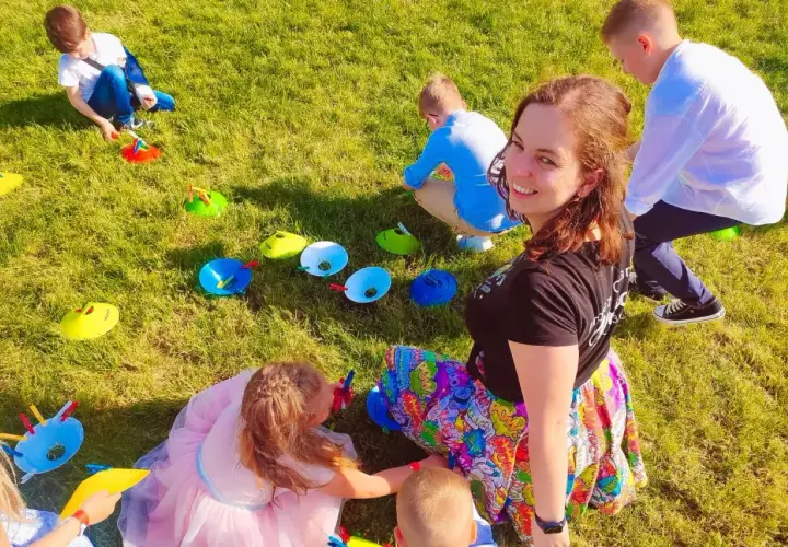 Uśmiechnięta animator dla dzieci cena. Dzieci bawią się na trawie, wykonując zadania z kolorowymi pachołkami.