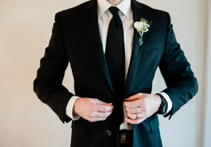 Elegancki czarny garnitur z butonierką, idealny jako jaki garnitur na wesele. Biała koszula i czarny krawat dopełniają stylizację.