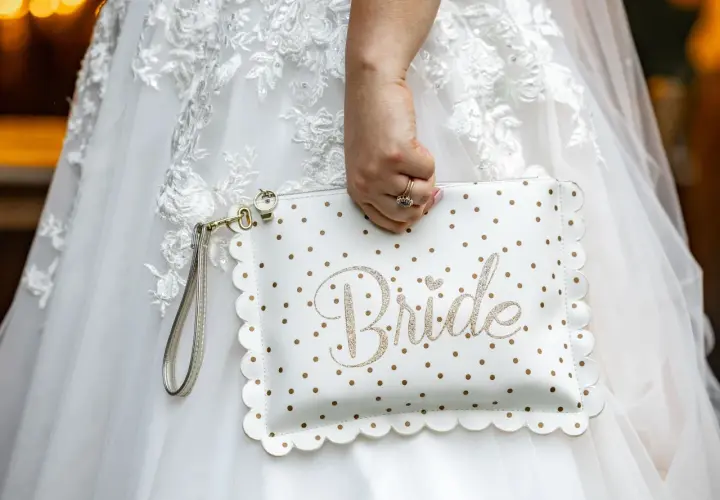 Biała kopertówka w złote kropki z napisem "Bride" to idealny niezbędnik pary młodej. Dopełnia suknię ślubną.