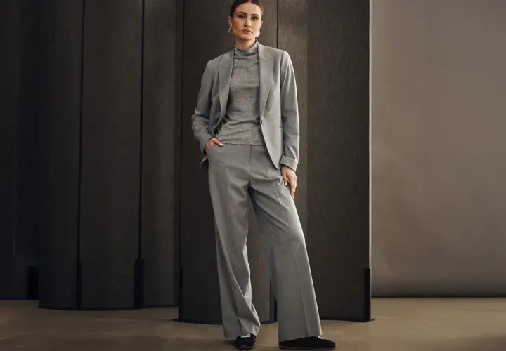 Elegancka kobieta w szarym garniturze, idealnym na wesele w spodniach. Stylowa i pewna siebie.