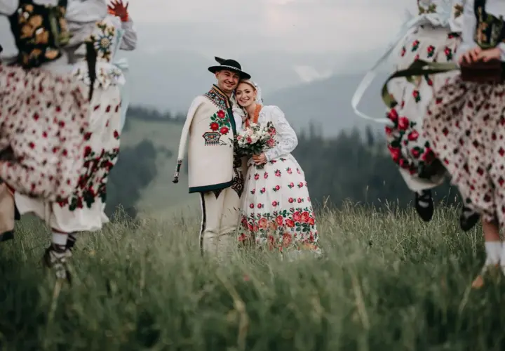 Para młoda w strojach góralskich z kapelą w tle, na tle górskiego krajobrazu.