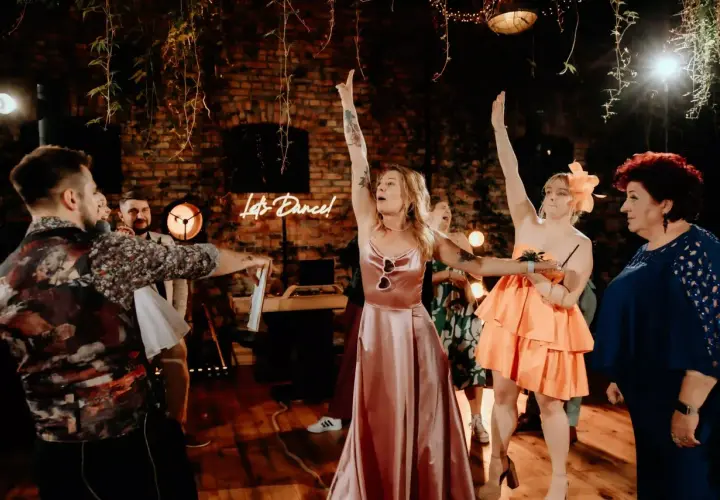 Radosny tłum świętuje oczepiny. Kobiety w pięknych sukniach unoszą ręce, a neonowy napis "Let's Dance!" zachęca do zabawy.