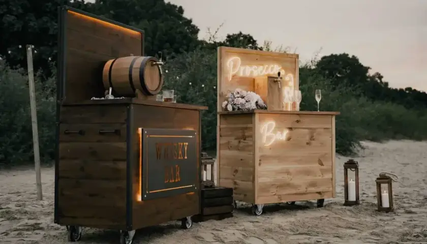 Drewniany shot bar z beczką whisky i neonowym napisem "Prosecco Bar" na plaży.