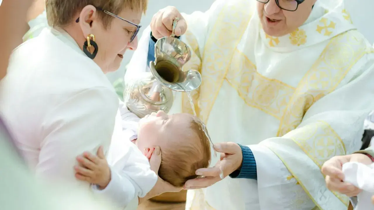 Chrzest dziecka. Kapłan polewa główkę niemowlęcia wodą święconą. Warto wiedzieć, ile kosztuje chrzest, by odpowiednio się przygotować.