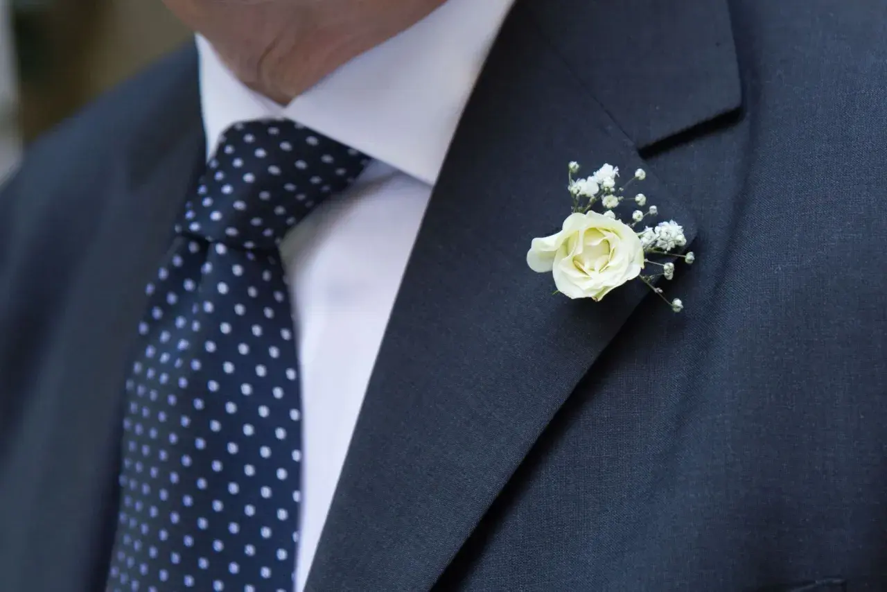 Elegancki garnitur z granatowym krawatem w kropki i delikatnym, białym kwiat w butonierce.