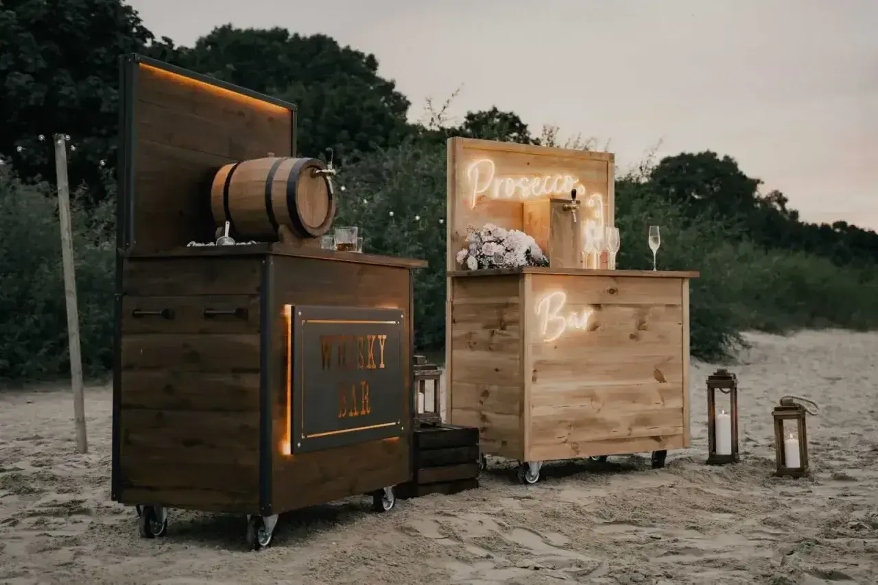 Drewniane, mobilne bary na wesele: jeden z beczką whisky, drugi z napisem "Prosecco Bar". Idealne na letnie przyjęcie.