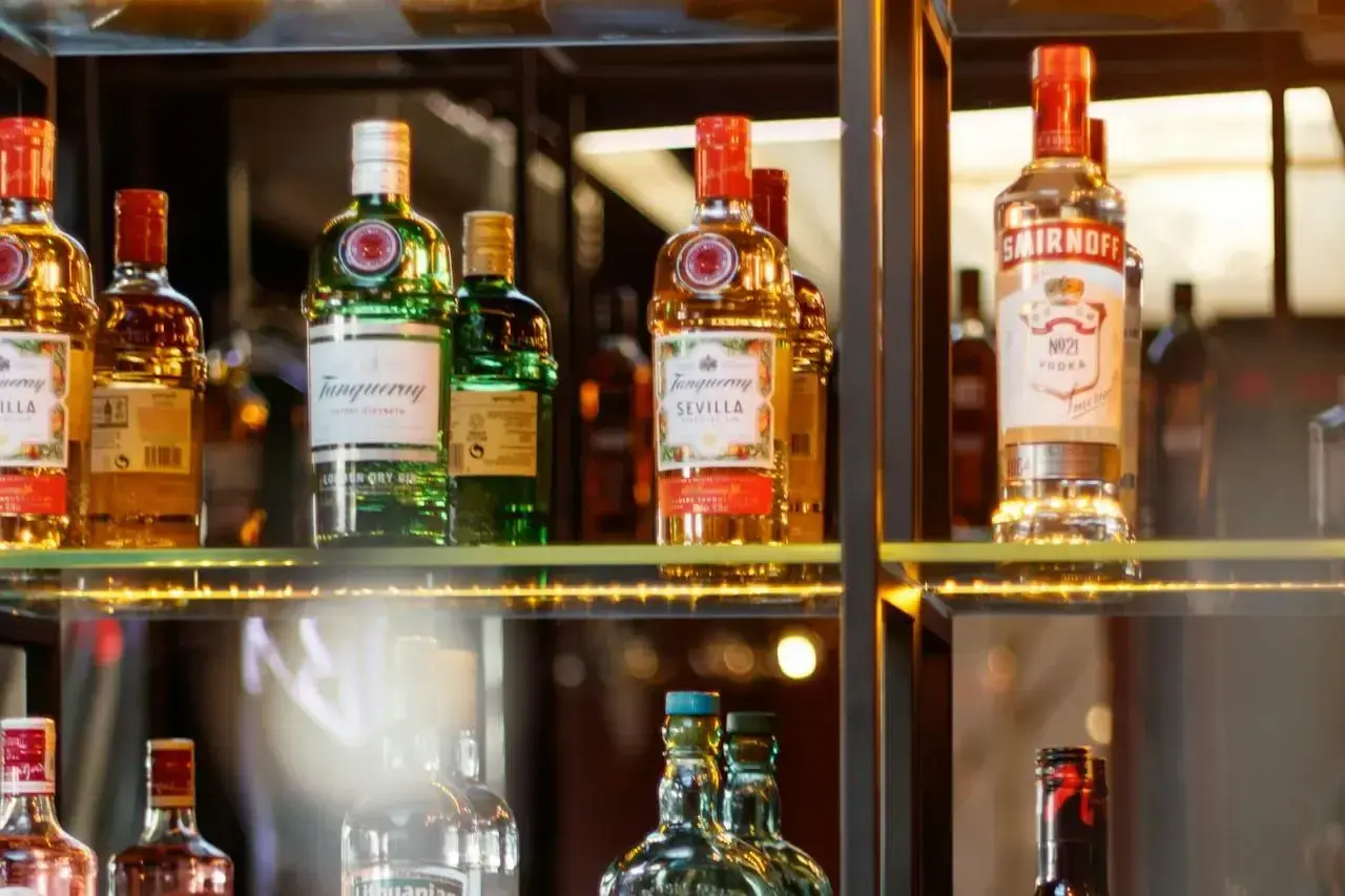 Butelki alkoholi na półce, w tym Tanqueray i Smirnoff. Idealne dla barmana na wesele, cena zależy od wyboru.