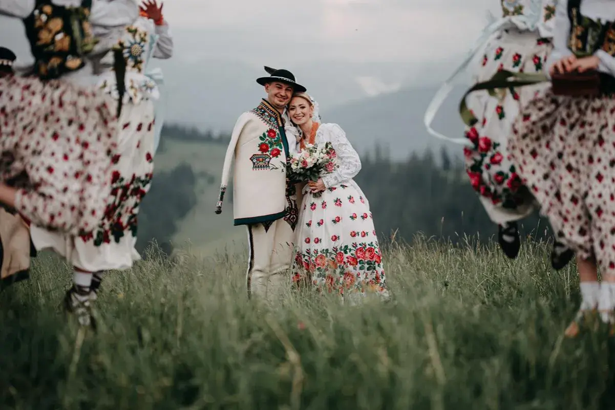 Para młoda w strojach góralskich z kapelą w tle, na tle górskiego krajobrazu.