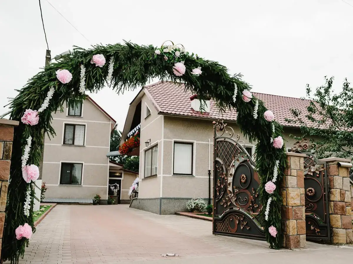 Piękne brama weselna pomysły: zielony łuk z różowymi kwiatami nad ozdobną bramą.