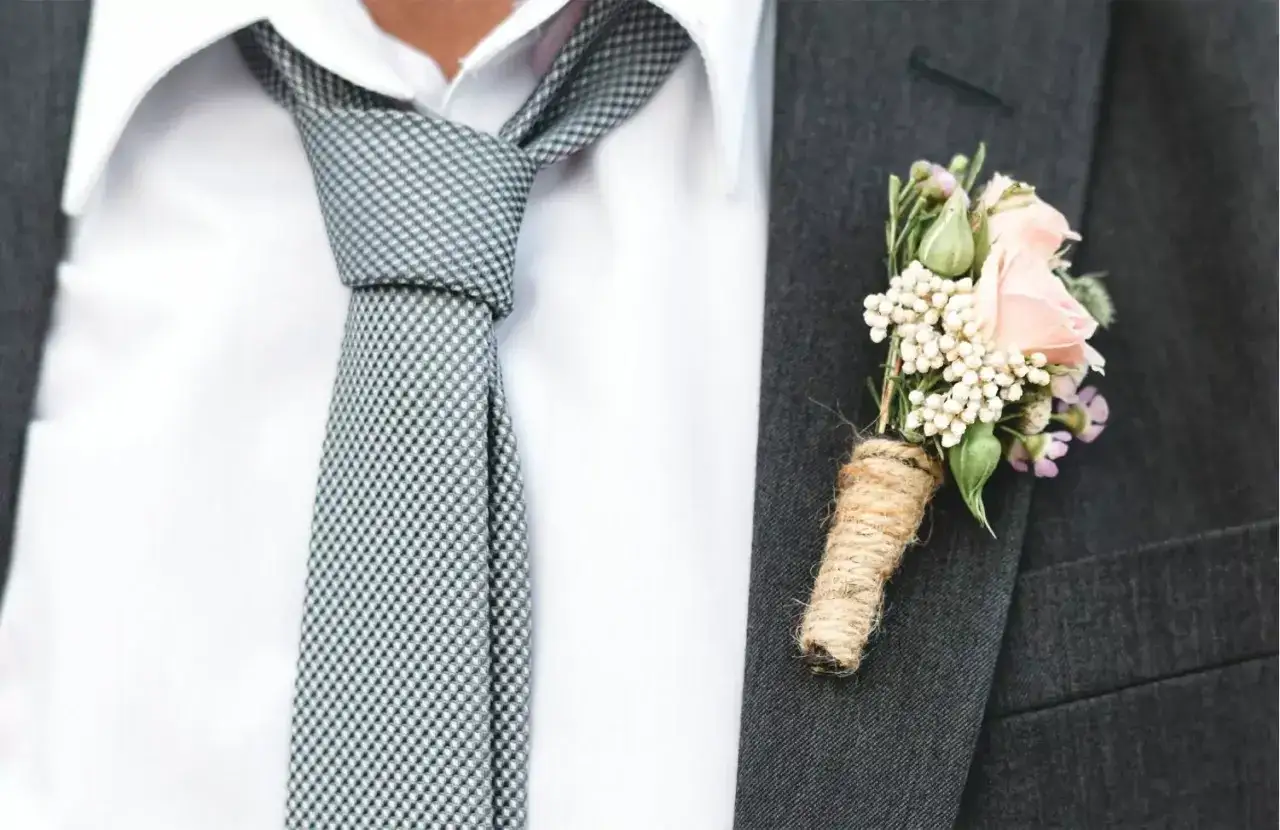 Elegancki garnitur z nietypowym wiązaniem krawata i bukiecikiem różowych kwiatów w butonierce.