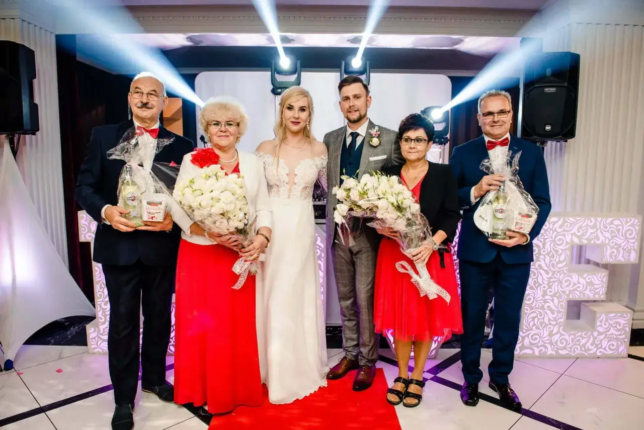 Para rodziców z bukietami i prezentami, jak na weselu, gdzie grają piosenki o rodzicach.