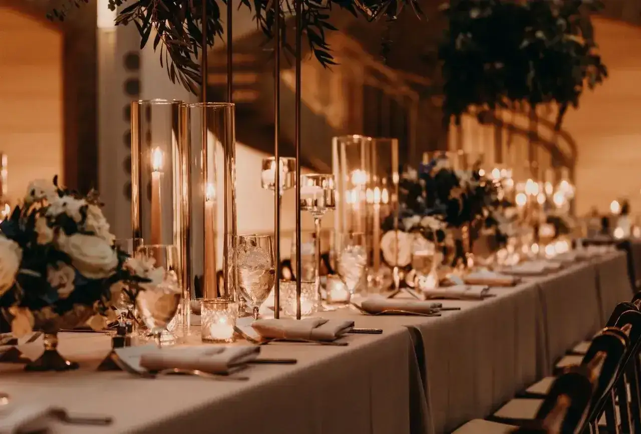 Elegancko nakryty stół weselny z kwiatami i świecami. Zastanawiasz się, ile kosztuje talerzyk na weselu?