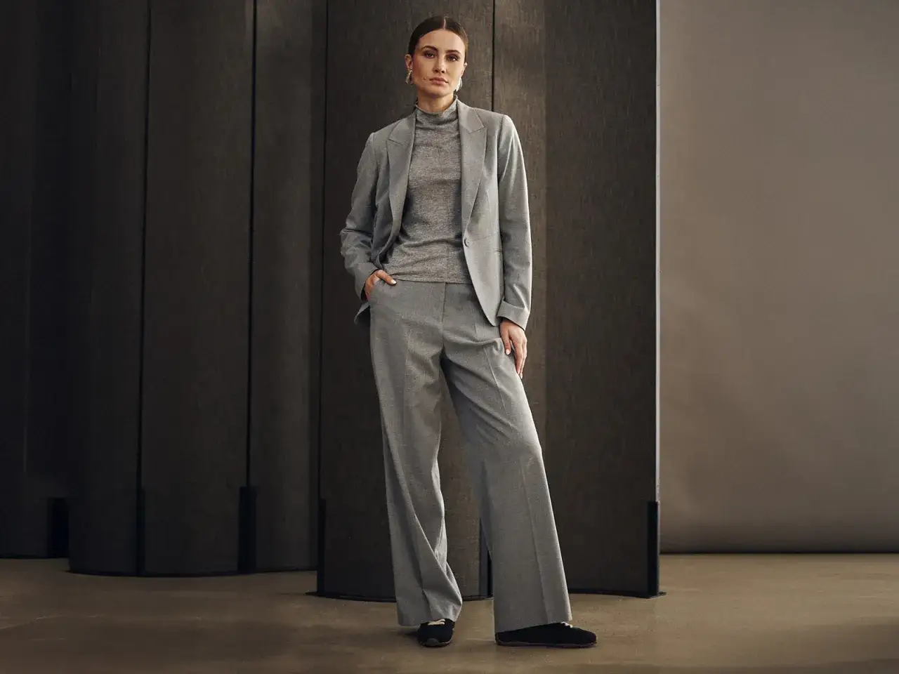 Elegancka kobieta w szarym garniturze, idealnym na wesele w spodniach. Stylowa i pewna siebie.